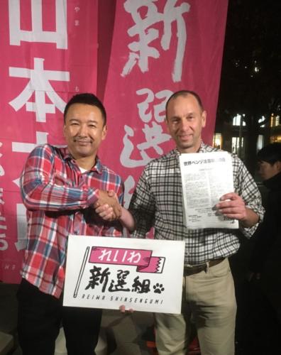 2019 - Wayne meets with Japanese politician - celebrity, Yamamoto Taro, at political rally with W-BAD pamphlet in hand